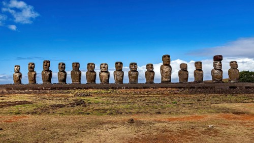 Row of Moai statues against a clear blue sky with scattered clouds, The Moai Statues on Easter