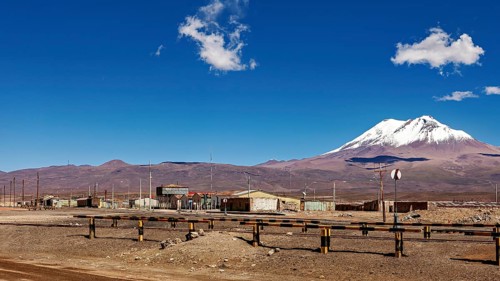 Scattered buildings under a snow-covered volcano in a dry landscape with clear skies, the town of