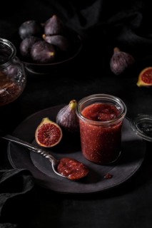 From above fresh fruit jam in small jar and on spoon with full and cut figs on plate at black