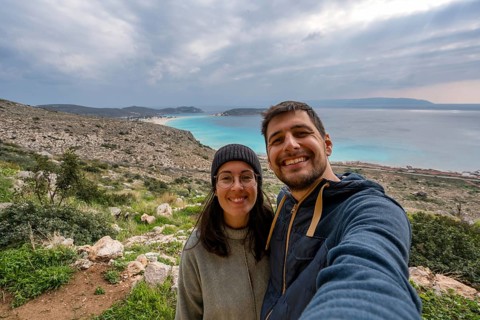 Happy couple taking a selfie with a stunning coastal backdrop in Greece. The vibrant turquoise sea,