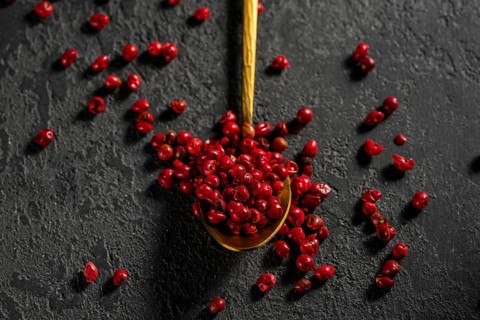 Top view of bright red peppercorns scattered from a golden spoon against a textured dark