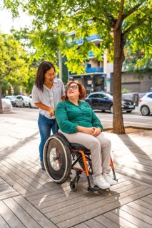 Asian caregiver pushing the wheelchair of a happy disabled woman along the city street