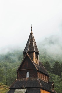 A stunning view of a Norwegian stave church surrounded by lush green forests and mist The