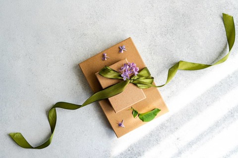 Two brown gift boxes adorned with a green ribbon and purple flowers are elegantly displayed on a