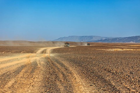 Car travelling on a dusty road through a vast landscape, mountains in the distance, Off-road