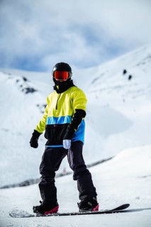 A snowboarder in vibrant gear stands on snowy slopes, ready for a downhill adventure in Andorra.