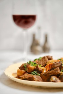 A plate holds a beef dish with vegetables. Nearby, a glass of red wine catches the light. The