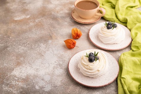 Pavlova Meringue dessert with crisp meringue and blueberry, cup of coffee, on brown concrete