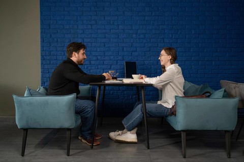 Two people are seated at a table in a cozy cafe, engaged in conversation over tea. They appear
