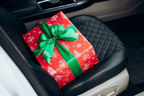 A vibrant red gift box wrapped with festive patterns and a green ribbon sits on a car seat,