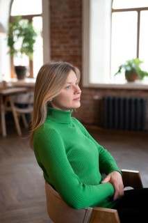 A young woman in a green sweater sits alone in a cozy cafe by the window, gazing thoughtfully