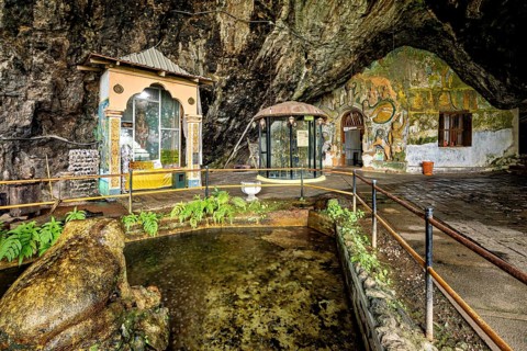 Interior of a cave with a small pond, sculptures and painted walls surrounded by vegetation, The