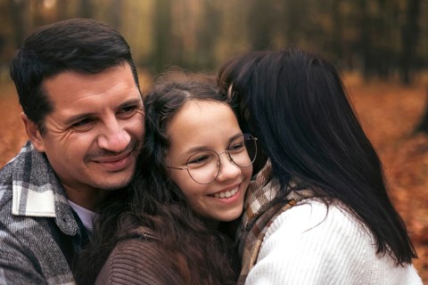 A family shares a joyful embrace surrounded by the warm hues of autumn foliage. The scene captures