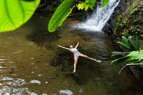 From above a young woman gracefully swimming in a natural pool under a waterfall in the Choco