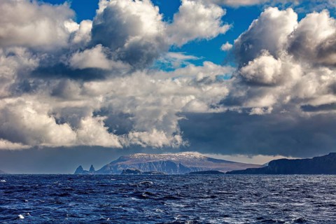 Dramatic clouds over a rocky island in the sea, with deep blue water under an impressive sky,