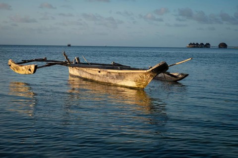 Traditional wooden outrigger boat floating on calm turquoise water during late afternoon light in