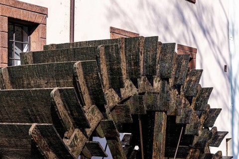 A close-up of a traditional wooden waterwheel against a historic Prague building, showcasing rich