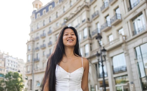 A cheerful Chinese woman with long hair wearing a white dress enjoys a sunny summer day in the