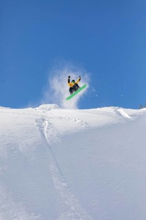 A snowboarder performs an aerial stunt on a snowy slope, set against a vibrant blue sky. The image