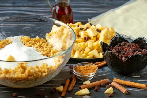 Bowl of sugar and breadcrumbs surrounded by apple pieces, cinnamon and raisins