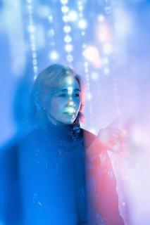 An elderly Asian woman interacts with a digital interface within the metaverse. She is surrounded
