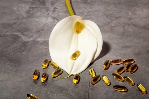 A refined composition featuring a pristine white calla lily alongside golden oil capsules on a
