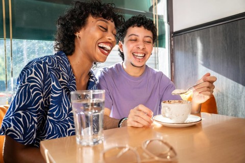 A multiethnic LGBTQ+ couple shares a joyful and intimate moment in a cozy cafe, laughing and