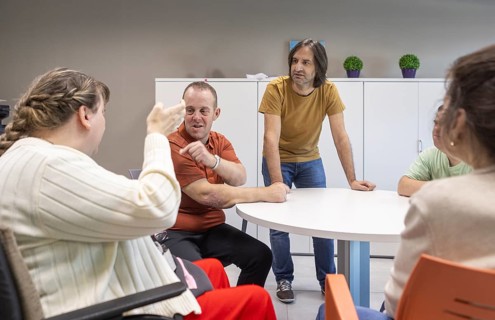 A group of people with mental disabilities engage in a discussion with a caregiver at a support