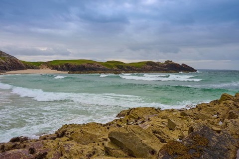 Waves meet rugged rocks on a dramatic coast, the sky is heavy with clouds, Clachtoll Beach,