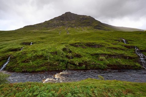 Lush greenery with small waterfalls and a mountain in the background under a cloudy ceiling, Glen