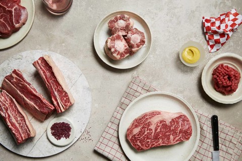 An assortment of fresh meats arranged on plates, showcasing different cuts like steak, oxtail, and