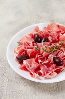 Freshly cut dried meat, served with olives and herbs, on a white plate, light background, no people