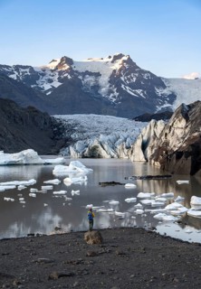 Hiker standing on a rock, reflection in the Svínafellslon glacier lagoon with ice floes,