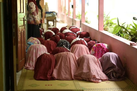 Back view of unrecognizable women dressed in traditional burqa and hijab kneeling in prayer, on a