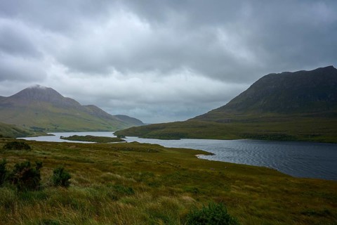 Grassy hills with a lake under a thick, cloudy sky, Loch Bad a Ghaill, Badnagyle, Ullapool,