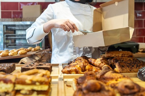 Baker wearing an apron and chef's jacket carefully placing a fresh baked item into a brown