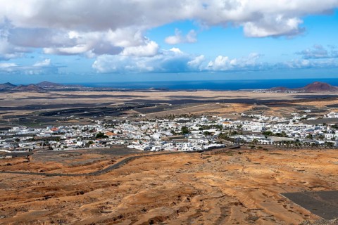 View of town, white houses of Teguise with church tower in dry volcanic landscape, view from