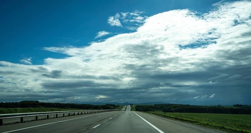 The road stretches into the distance under a dramatic sky filled with clouds, showcasing the