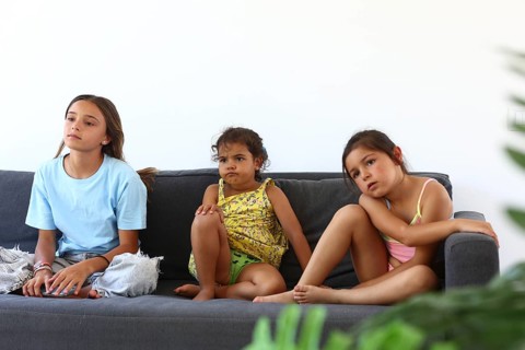 Friends sit on a cozy gray sofa in a bright living room. They appear relaxed and focused,