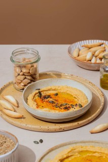 Creamy hummus garnished with seeds and spices, served on a rustic plate with breadsticks. A jar of