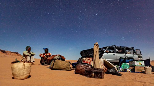 Night in the desert with two people next to a car full of luggage under a clear starry sky, Tuareg