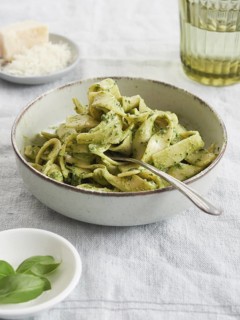 Close-up of green pasta bowl with fork on green Tagliatelle pesto beside basil leaves and parmesan