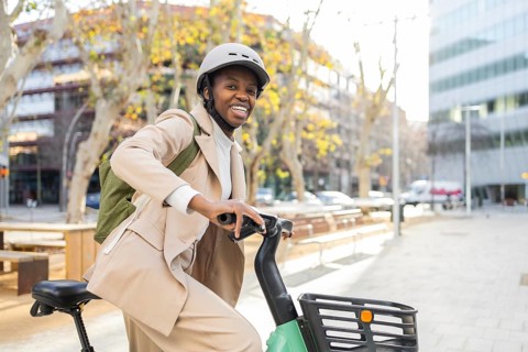 A smiling black woman in urban attire rides a bike, embodying joy and freedom The city street