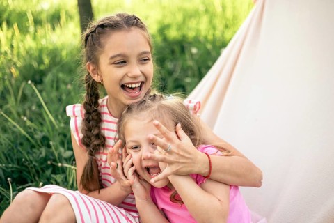 Two young sisters share a moment of joy, laughing and playing together in a lush outdoor field Her