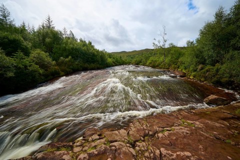 A shallow, fast-moving river in a forest scene under cloudy sky, Victoria Falls, Slattadale,