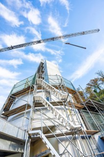 Scaffolding with metal stairs in front of a blue sky with crane, construction work in progress,