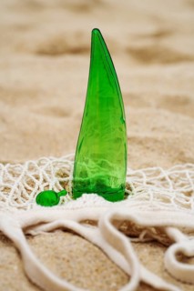 A green aloe vera gel bottle with a matching capsule lies on a beige, sandy background, intertwined