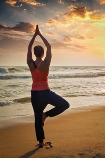 Yoga outdoors, sporty fit woman doing Hatha yoga asana Vrikshasana tre pose on tropical beach on