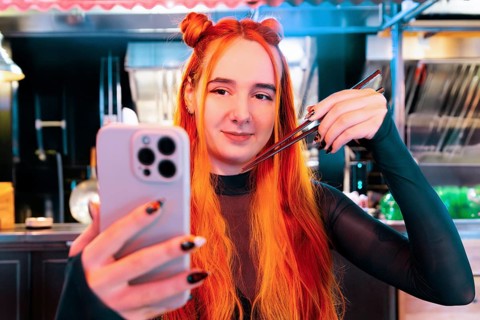 A woman with vibrant hair takes a selfie at an Asian food market, capturing her experience with
