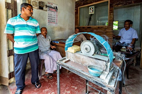 Several men are standing or sitting in a room and looking at a grinding machine, the gemstone